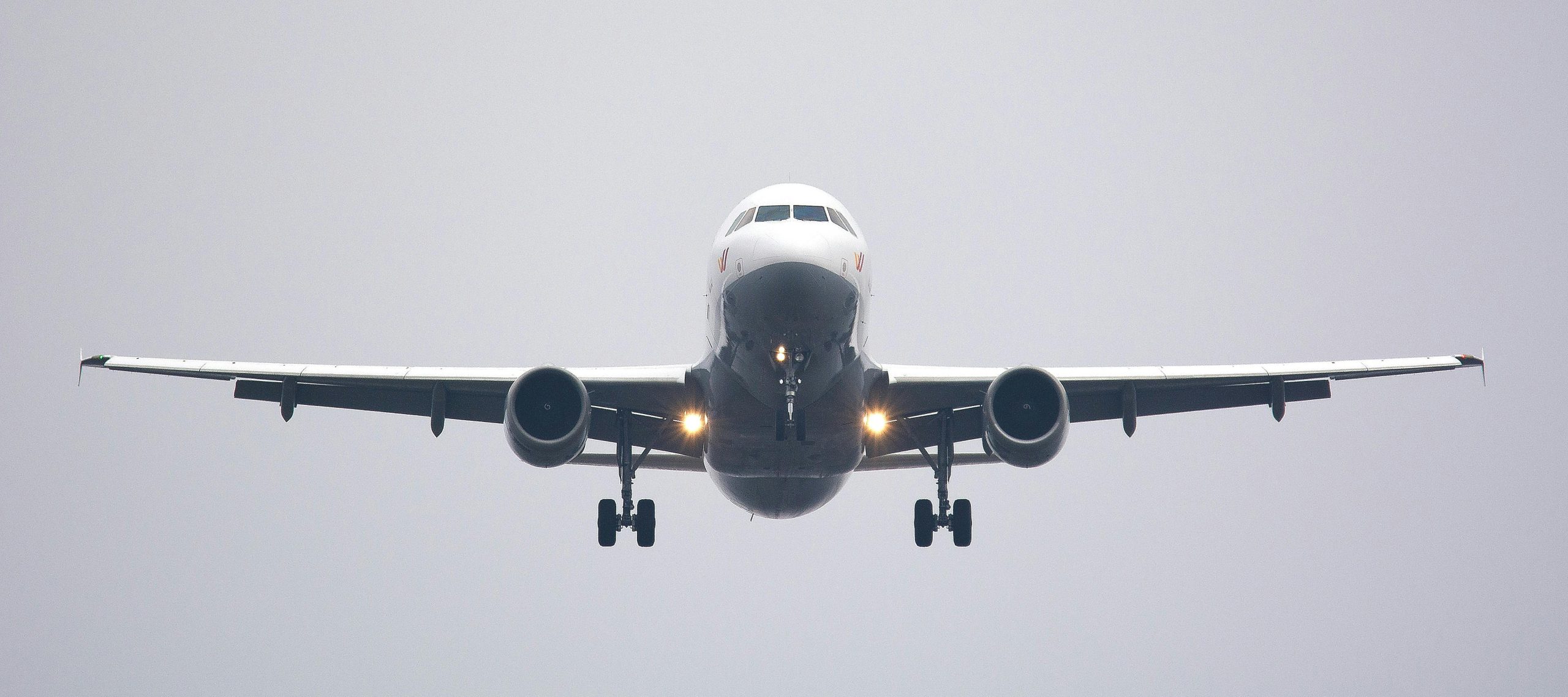 A commercial airliner captured head-on, preparing to land against a cloudy sky.